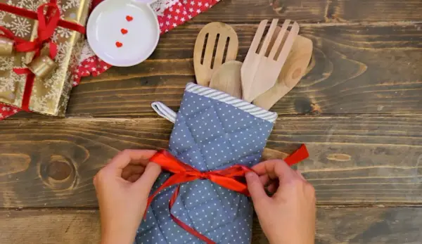 Idee regalo fai da te: un set di utensili da cucina in legno, avvolto in un guanto da forno a pois e legato con un nastro rosso.